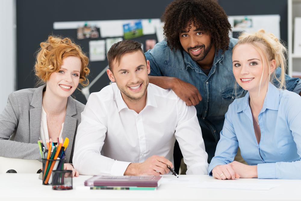 Diverse multiracial young business team in a creative office posing close together behind a desk in the office smiling at the camera-1